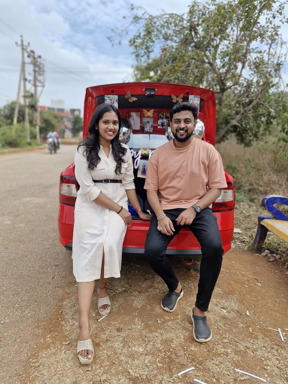 Navya and Subramanya sitting on the boot of a red car