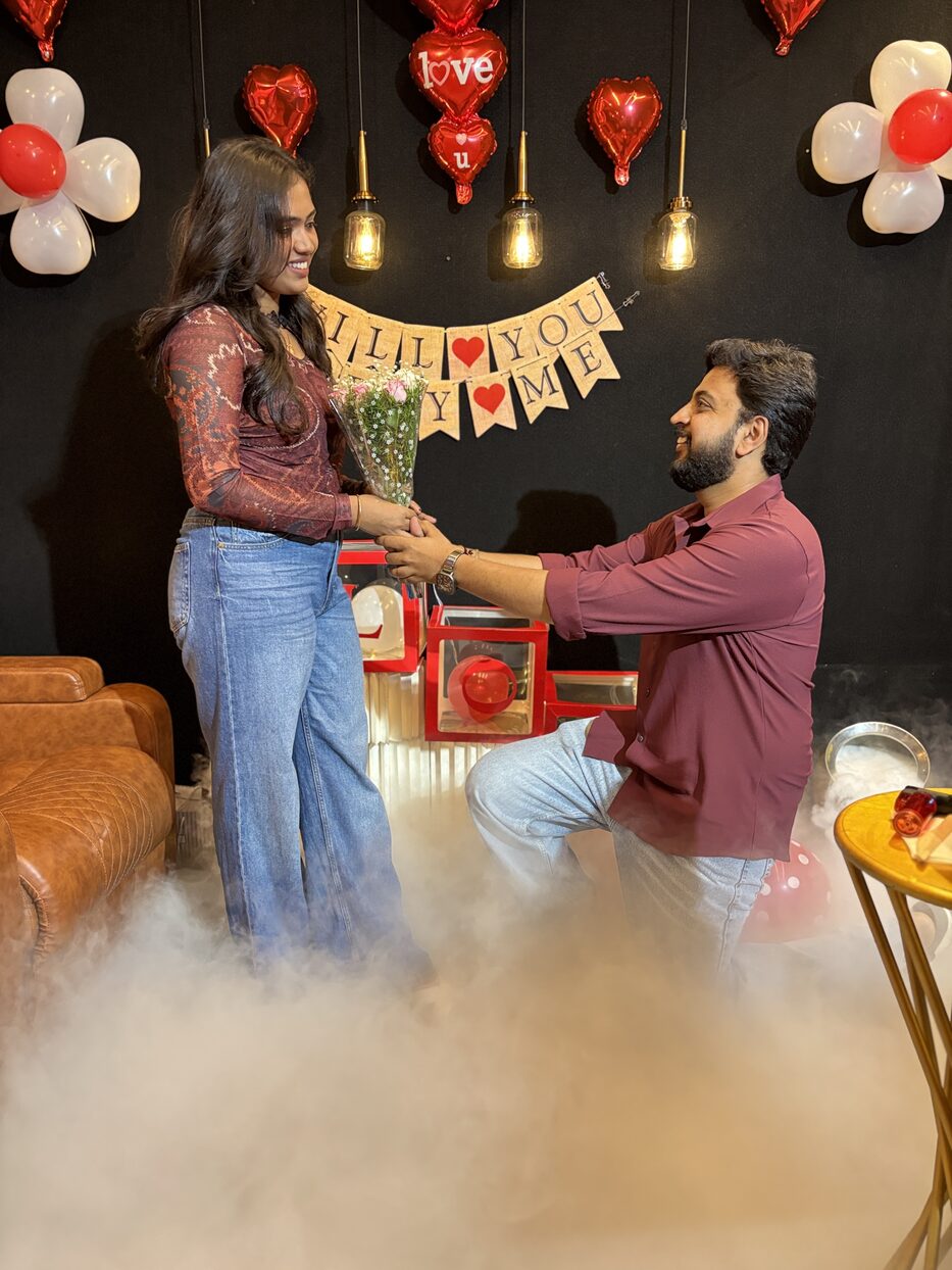Subramanya on one knee proposing to Navya with a bouquet